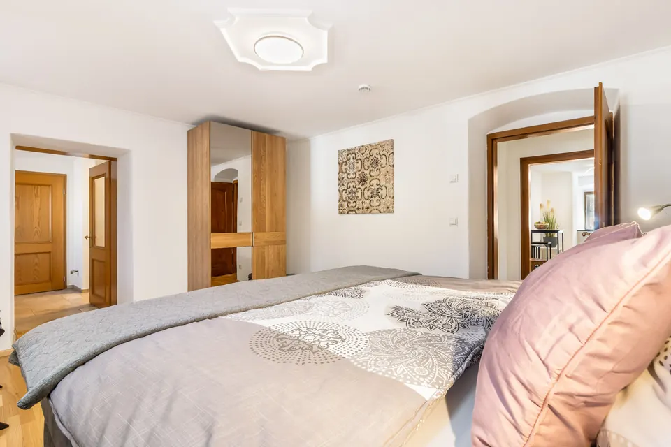 Schlafzimmer mit Boxspringbett, rosa Kissen und Holzschrank