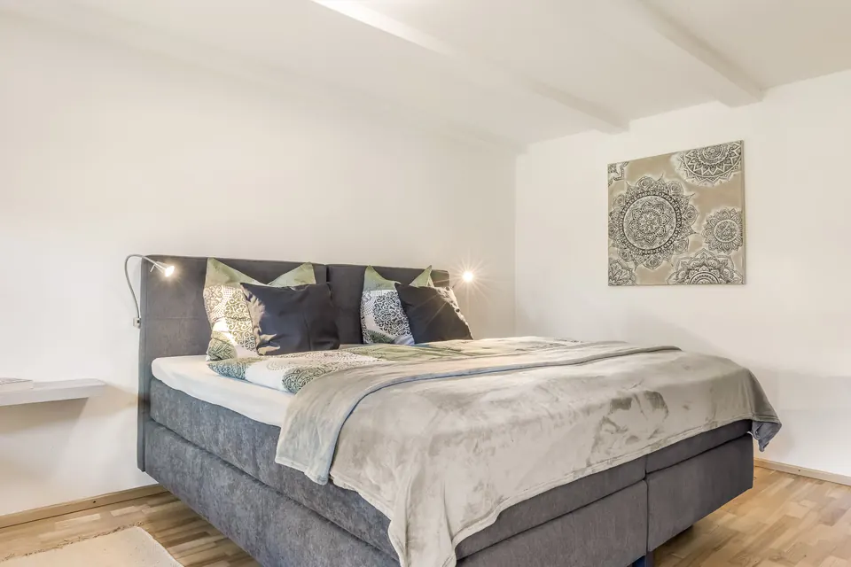Schlafzimmer mit Boxspringbett, grauer Tagesdecke und Leselampen