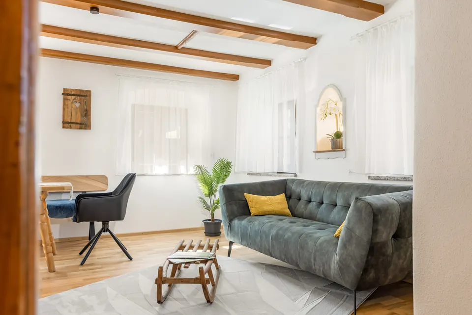 Wohnzimmer der Ferienwohnung am Samerberg mit Holzbalken, grünem Samtsofa und Essplatz im Tageslicht